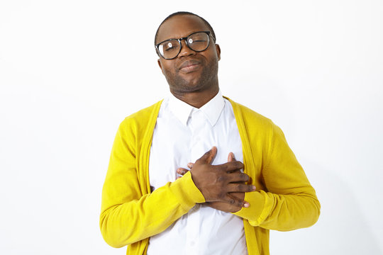 Friendly looking grateful Afro American man keeping hands on his chest, showing sympathy, acknowledgement and gratitude, being in high spirits or flattered. Positive human emotions and body language