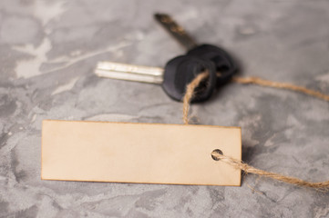 Blank rectangle paper and rope tied to two shiny metal keys with black plastic handle on old gray dirty cement floor with copy space. Estate concept