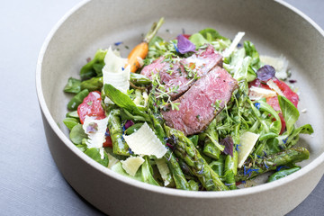 Modern spring salad with barbecue dry aged sliced fillet steak and green asparagus as top view on a plate