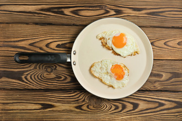 Two fried eggs in metal beige pan on old wooden brown table. Top view