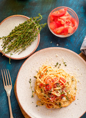 Spaghetti with tomatoes and thyme in a plate on a blue table.  Top view