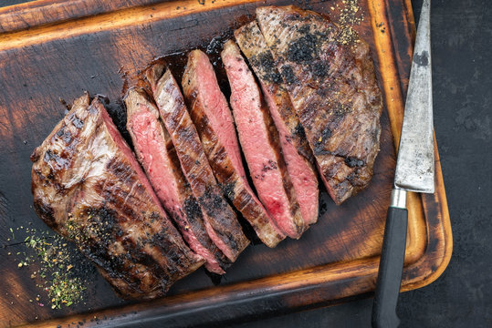 Barbecue Dry Aged Wagyu Flank Steak Sliced As Top View On A Burnt Cutting With A Knife