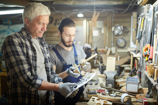 Mature professional measuring workpiece sketch on paper with his trainee near by - Powered by Adobe