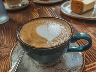 Cup of cappuccino with latte art on a brown wooden background. Stylish foam, retro cup of coffee in a coffee shop, copy space