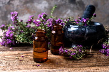 thyme essential oil on a  bottle, mortar and fresh thyme bunch  on a wooden table