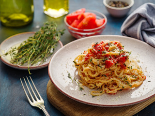 Spaghetti with tomatoes and thyme in a plate on a blue table