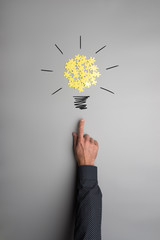 Hand of a businessman pointing on a light bulb made of yellow puzzle pieces