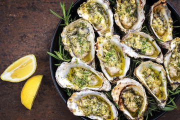 Barbecue overbaked fresh opened oyster with garlic, lemon and herbs offered as top view on a tray