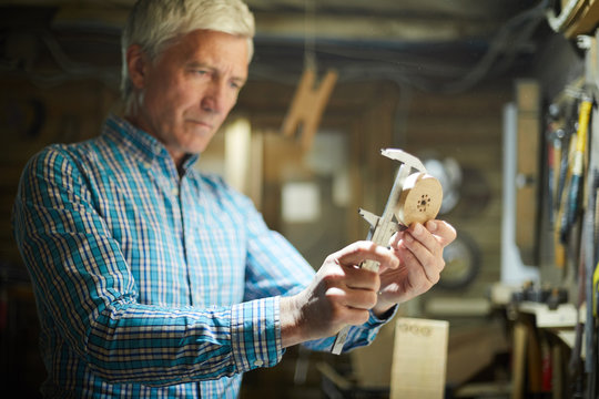 Professional engineer measuring diameter of round wooden workpiece in his workroom - Powered by Adobe