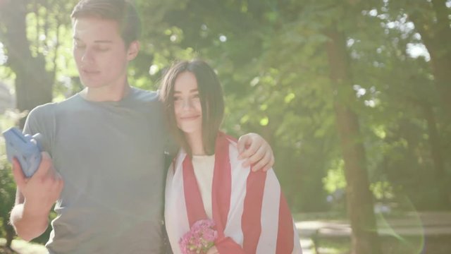 Charming couple walk feel happy man take photo woman with American flag in park sunset sunlight slow motion caucasian family havingfun cheerful lovers outdoors young fun boyfriend city friendship date