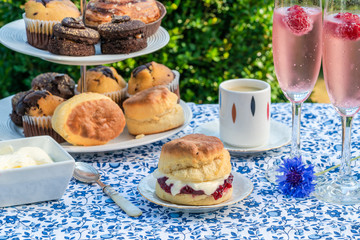 Afternoon tea with cakes and traditional English scones with strawberry jam and clotted cream set up on a table in the garden. Outdoor dining.
