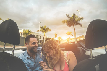 Happy millennial couple having fun in convertible car in summer vacation - Young people laughing on...