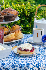 Afternoon tea with cakes and traditional English scones with strawberry jam and clotted cream set up on a table in the garden. Outdoor dining.