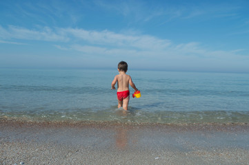 a small child boldly enters the sea. in the arms of the baby toy watering can.