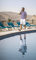 middle aged arab man by a pool, talking on a phone
