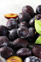 Plums on white stone background. Half of blue plum fruit. Many beautiful plums with leaves.