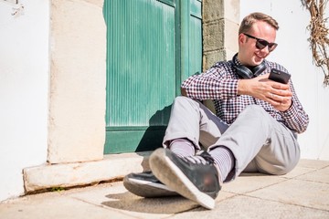 Young guy with sunglasses, headphone and smartphone sitting on the pavement