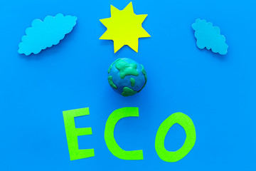 Eco icon cutout near plastiline symbol of planet Earth, sun, clouds on blue background top view copy space