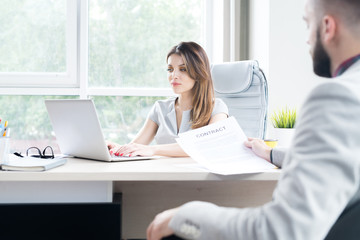 Portrait of modern female boss sitting at desk in big office and using laptop during meeting with client
