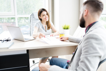 Portrait of modern female boss sitting at desk in big office smiling happily offering contract to client