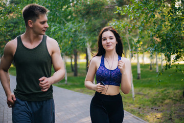 A young girl and a guy are running around the park. Doing sports outdoors. People in sportswear make a run. Leisure