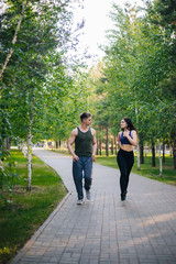 Fototapeta na wymiar A young girl and a guy are running around the park. Doing sports outdoors. People in sportswear make a run. Leisure