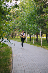 Obraz premium Young beautiful girl on a run. A woman is engaged in sports in the park. Healthy lifestyle. Running along the path with headphones, listening to music.