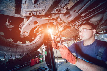 Car mechanic examining car suspension of lifted automobile at repair service station