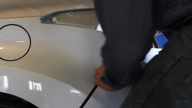 Man puts a bumper and a tail light on a newer car and then closes the trunk. Filmed inside of an automotive repair facility.