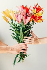 Man's hand giving bouquet of flowers to woma's hand on white background