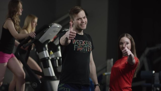 strict coach and pretty brown hair girl with straight hair in a red t-shirt approuve with thumbs-up with people engaged in simulators in the background