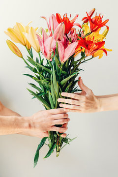 Man's Hand Giving Bouquet Of Flowers To Woma's Hand On White Background