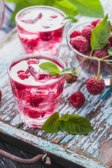 Red raspberries cocktail with ice and fresh mint on a old wooden table