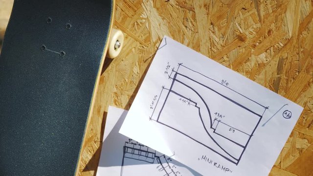 view of a new skateboard on a wooden background with plans for a miniramp in a skatepark in the summer