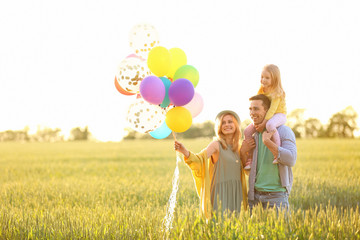 Happy family with colorful balloons in field on sunny day