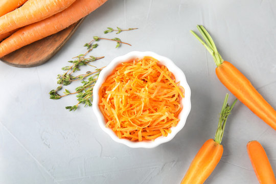 Bowl with grated ripe carrot and fresh vegetable on table, top view