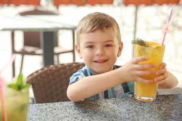 Cute boy with glass of natural lemonade at table in cafe