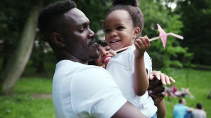 Portrait young african father hugging his daughter play holds on hands twists spending holiday together in park family affection smile slow motion child summer man kid sun girl parenting outdoors - Powered by Adobe