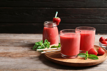 Glasses with tasty strawberry smoothie on wooden plate