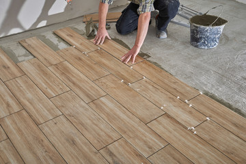 Hands of the tiler are laying the ceramic wood effect tiles on the floor