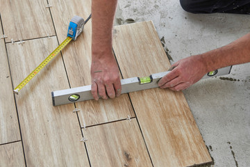 Laying wood effect tiles on the floor. Worker laying floor tiles.