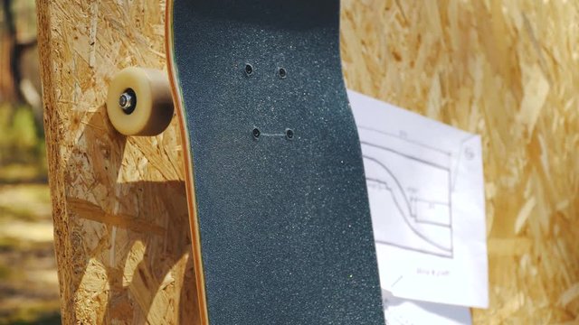 view of a new skateboard on a wooden background with plans for a miniramp in a skatepark in the summer