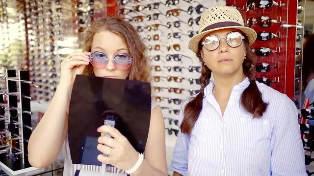 Beautiful adult women want to buy new sunglasses on outdoor market.
