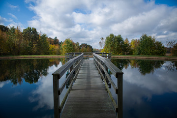 A wooden pier over a still lake in the middle of the woods in fall