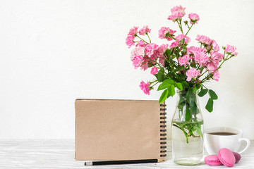 creative mock up with a beautiful bouquet of pink roses flowers, coffee cup, macaroons and blank hipster notebook