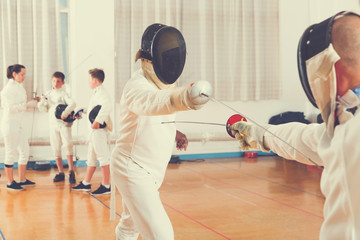 Adults and teens wearing fencing uniform practicing with foil