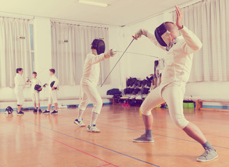 Adults and teens wearing fencing uniform practicing with foil