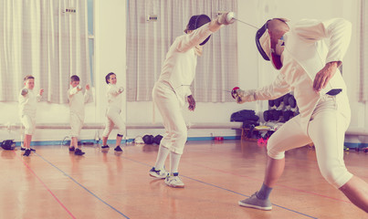 Obraz premium Adults and teens wearing fencing uniform practicing with foil