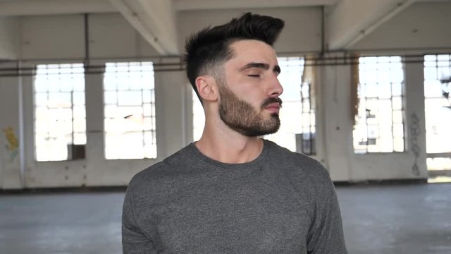 Young man joking, doing stupid expression with his tongue for the camera in a big empty room, acting silly