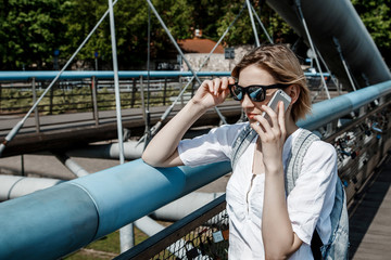Stylish girl near the Vistula River in Krakow. Bridge across the river in Krakow. Young woman in town. Lady with a mobile phone. Travel to Poland.